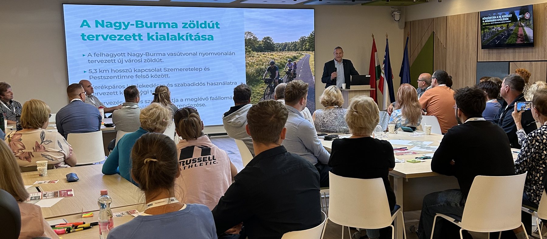 Lakossági közösségi gyűlés a XVIII. kerületben: a résztvevők asztaloknál ülve hallgatják a Nagy-Burma zöldút tervének bemutatását